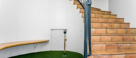 A staircase with a blue handrail, a wooden bench, and a green artificial turf area with golf equipment.