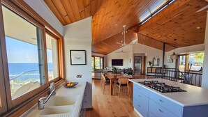 Una cocina moderna con una isla grande, techo de madera y vista al océano.