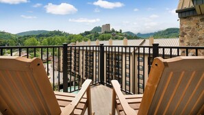 A balcony with wooden chairs, a stone building, and a view of a mountain and a tall building in the distance.