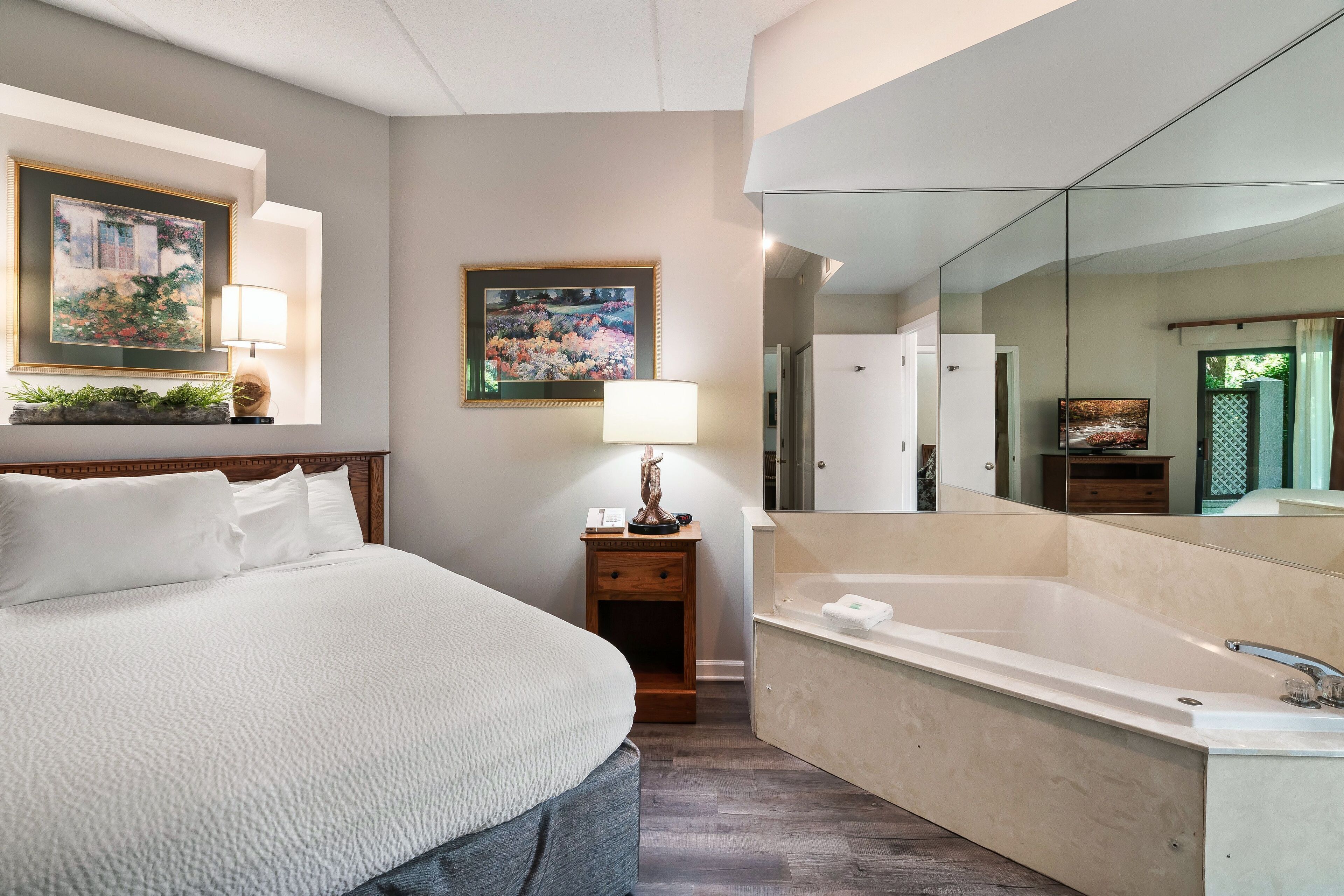 Ein modernes Hotelzimmer mit einem großen Bett, einer Sitzecke mit einer Lampe, einem großen Spiegel und einer Badewanne.