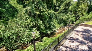 Un chemin pavé longe un ruisseau, bordé d’une végétation luxuriante et délimité par une rambarde métallique.