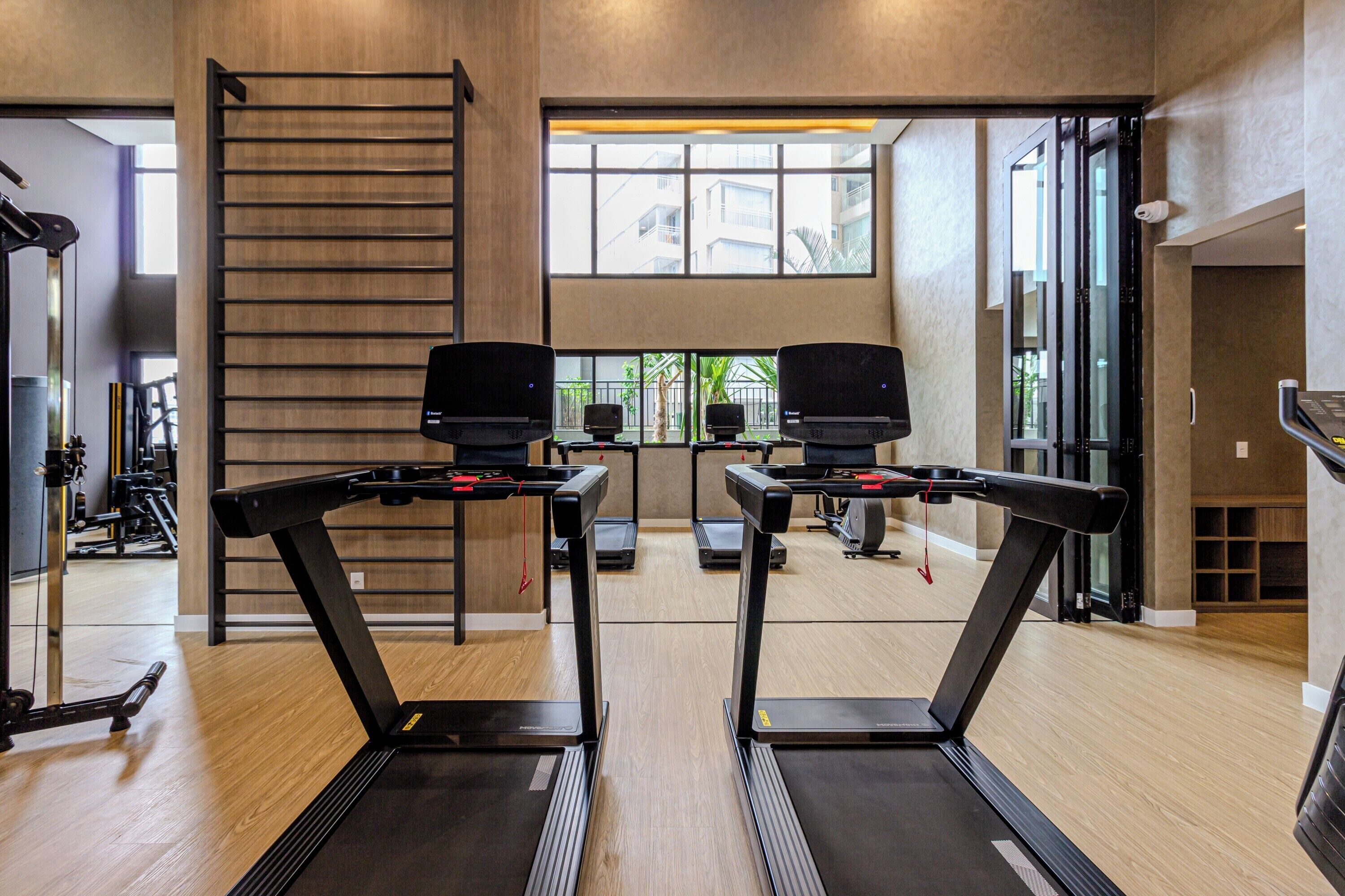 A gym with two treadmills, a wooden floor, a large window, and a staircase.