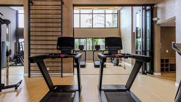 A gym with two treadmills, a wooden floor, a large window, and a staircase.