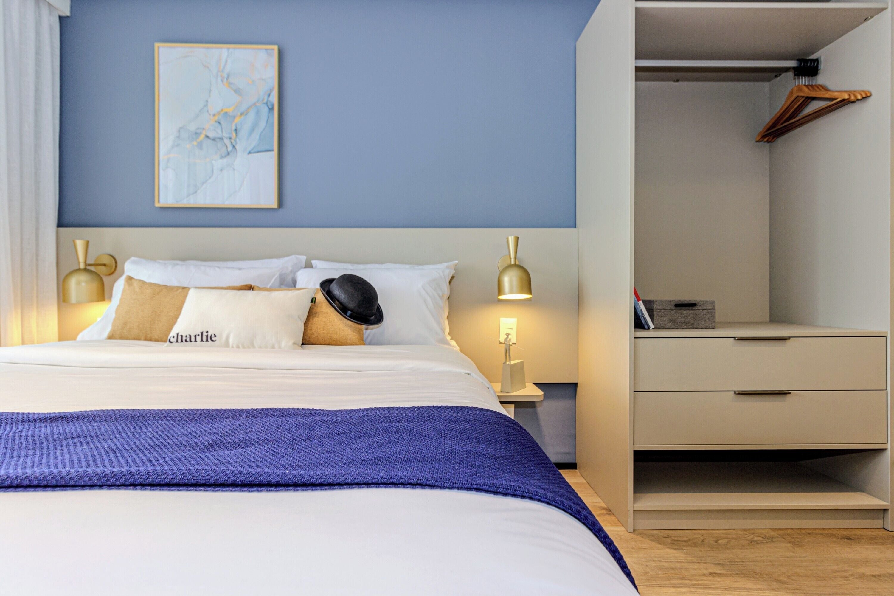 A neatly made bed with a blue blanket, a bedside lamp, and a nightstand with a book and a box.