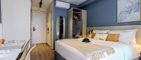 A bedroom with a bed, a wardrobe, a mirror, and a dining area.