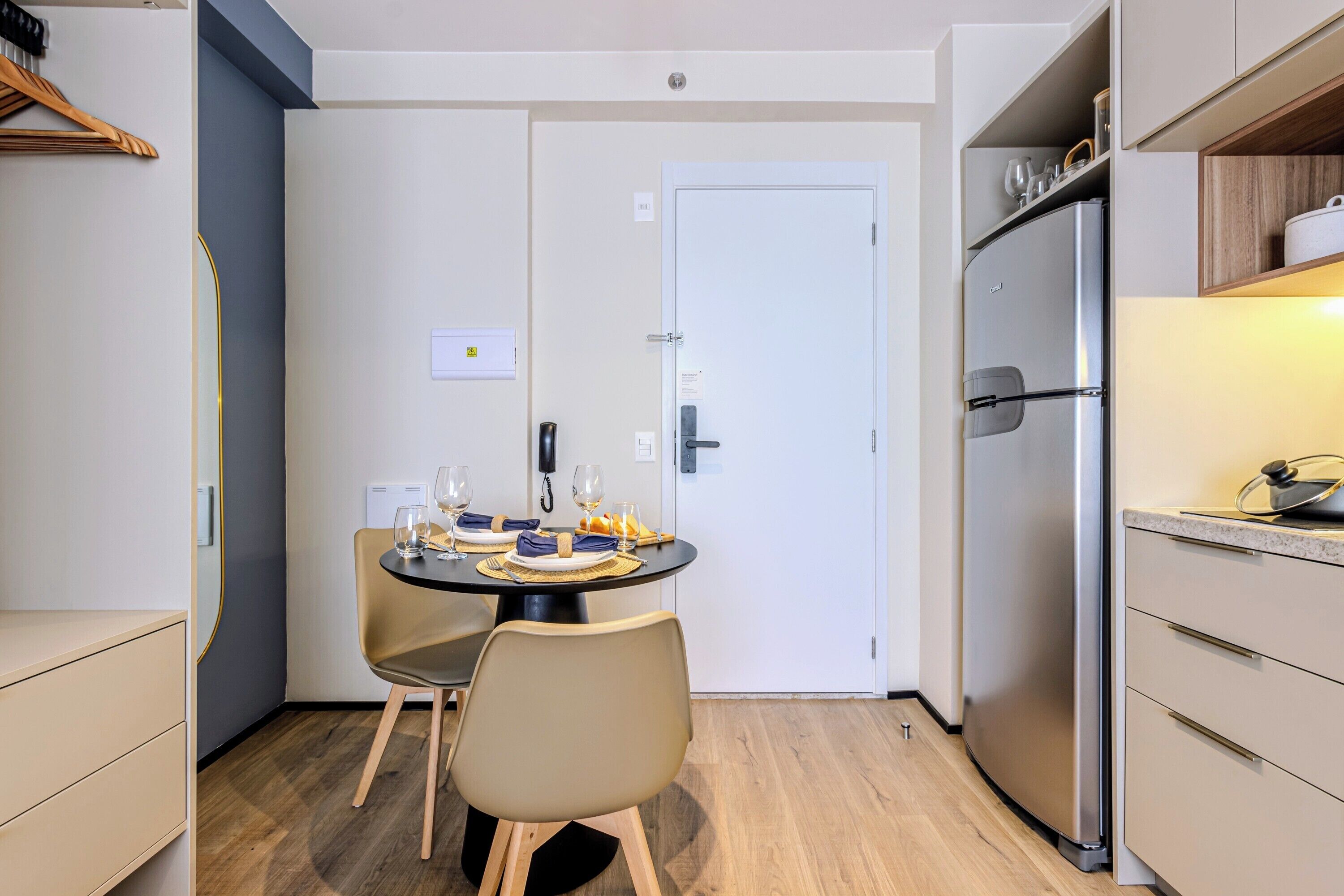 Une cuisine compacte comprenant un coin repas, un réfrigérateur et une porte dotée d’un interrupteur pour la lumière.