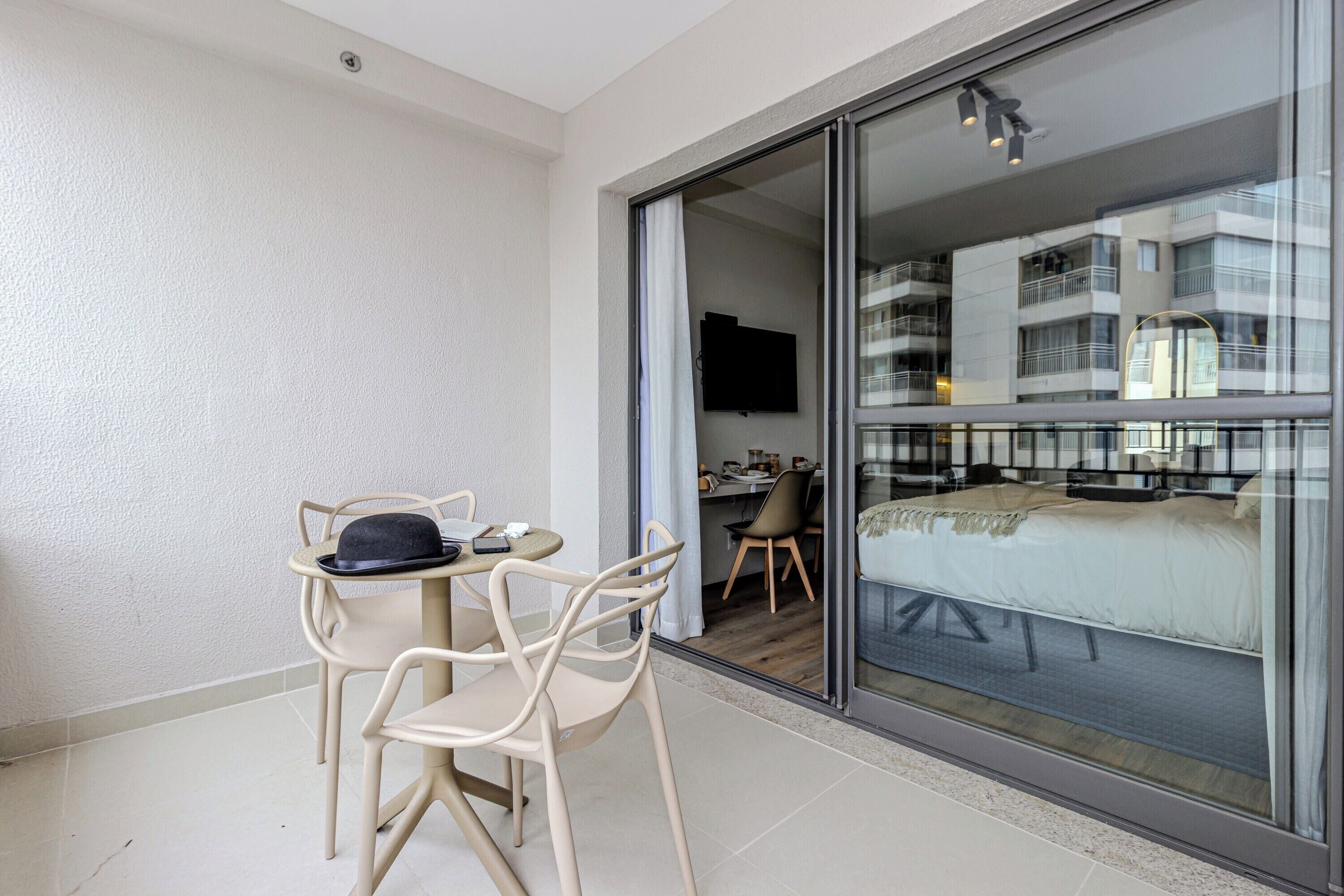 A balcony with a table and chairs, a bed, and a TV in the adjacent room.