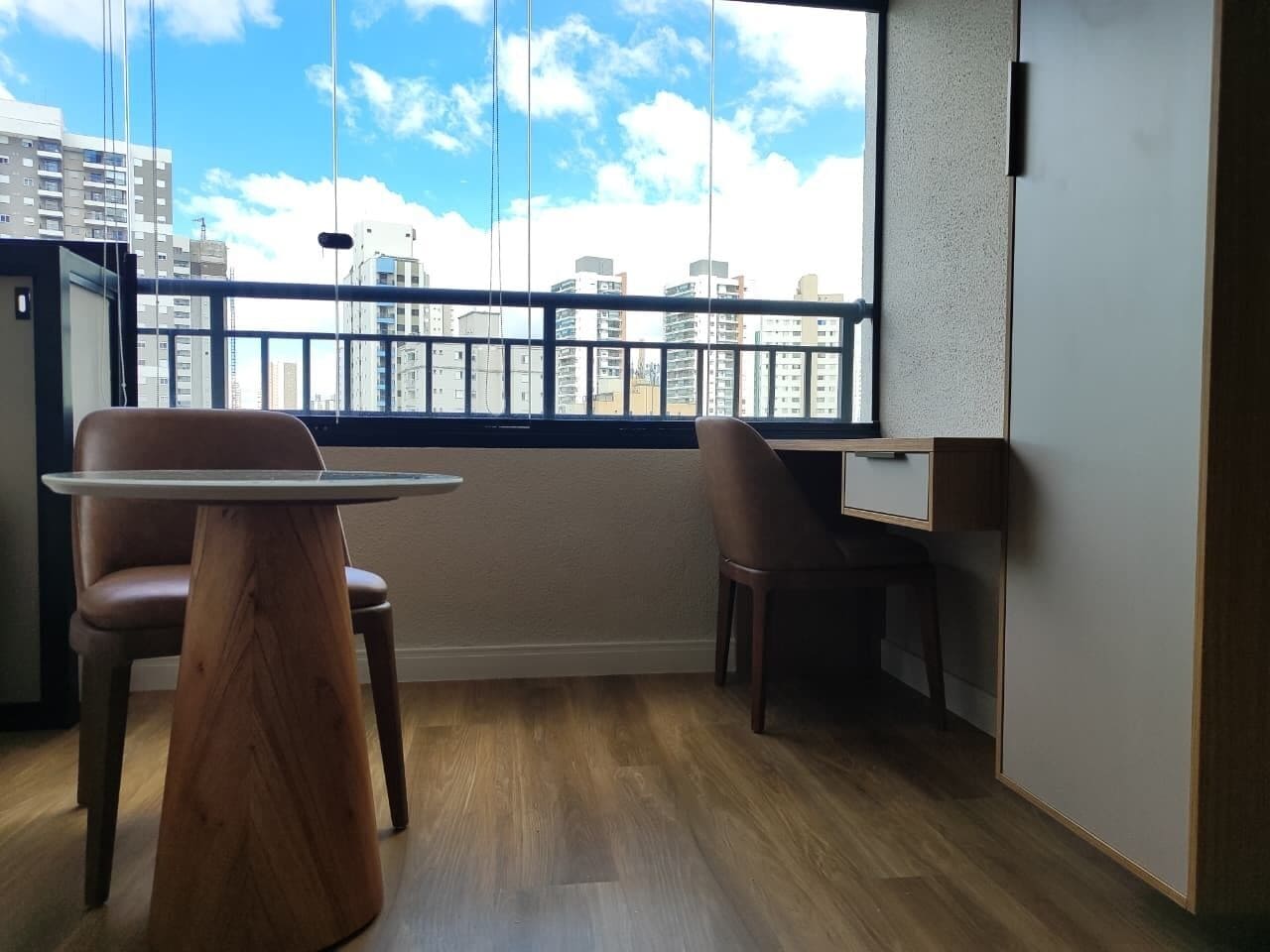 A modern room with a large window, a wooden table, two chairs, and a desk.