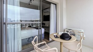 Ein Hotelzimmer mit einem Bett, einer Schiebetür zu einem Balkon, einem kleinen runden Tisch mit Hut und Smartphone sowie einem Stuhl.