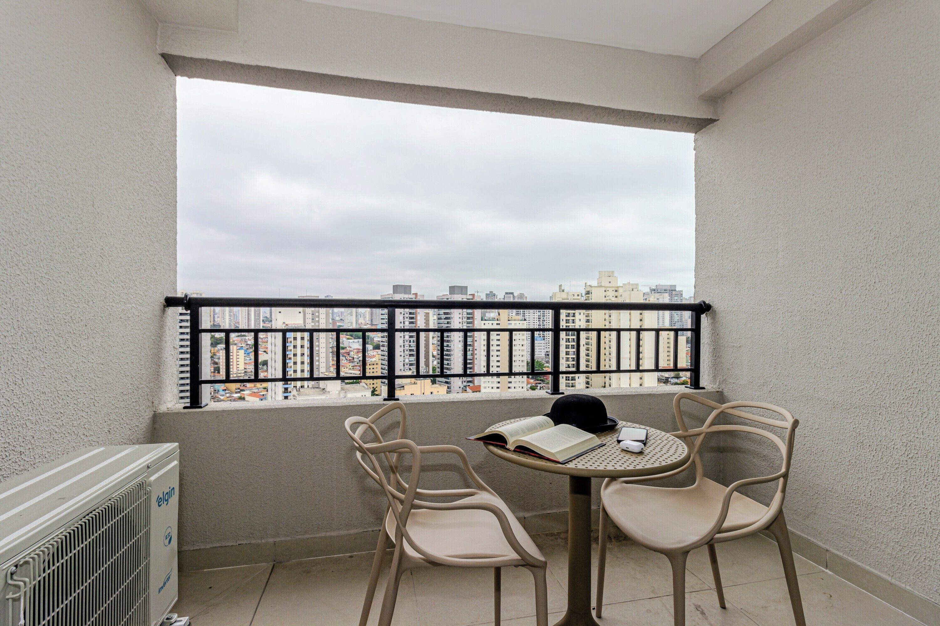 A balcony with a view of a cityscape, two chairs, a table, and a radiator.