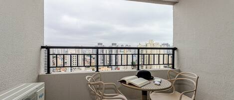 A balcony with a view of a cityscape, two chairs, a table, and a radiator.