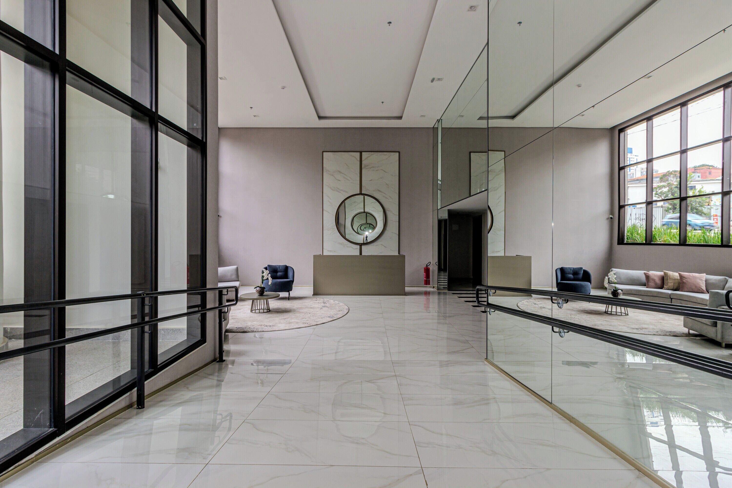 Un hall d’entrée spacieux au design moderne, doté d’une grande rambarde en verre, d’un élément décoratif circulaire central et d’espaces de détente avec des canapés et des fauteuils.