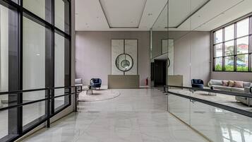 Un hall d’entrée spacieux au design moderne, doté d’une grande rambarde en verre, d’un élément décoratif circulaire central et d’espaces de détente avec des canapés et des fauteuils.