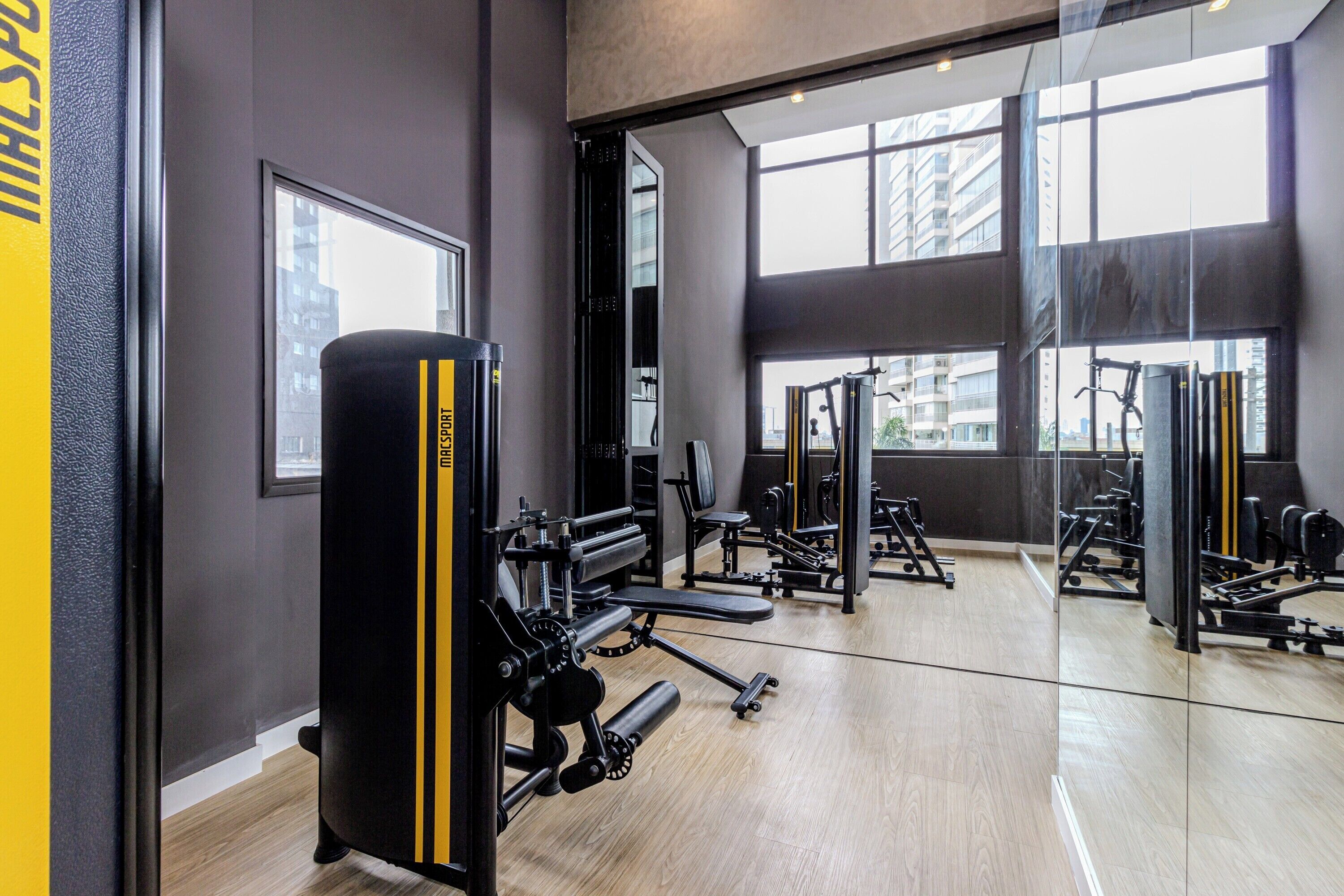 A gym with various exercise equipment, large windows, and a mirror reflecting the equipment.