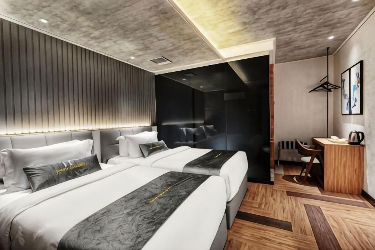 A modern hotel room with two beds, a desk, and a seating area.