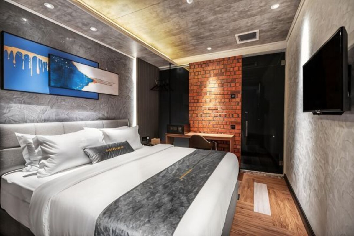 A modern bedroom with a bed, a desk, and a TV.