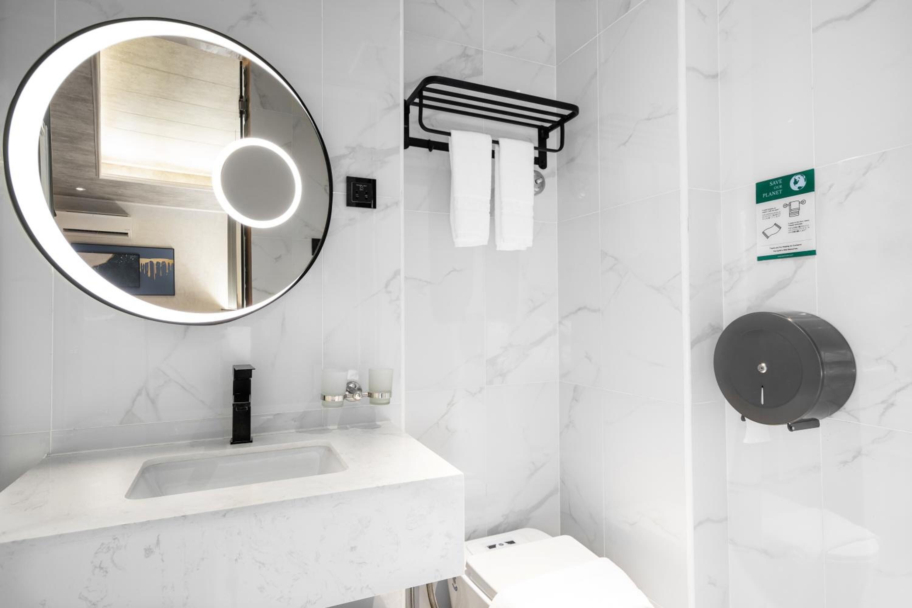 Ein modernes Badezimmer mit rundem Spiegel, Waschbecken, Handtuchhalter und einem Handtrockner.