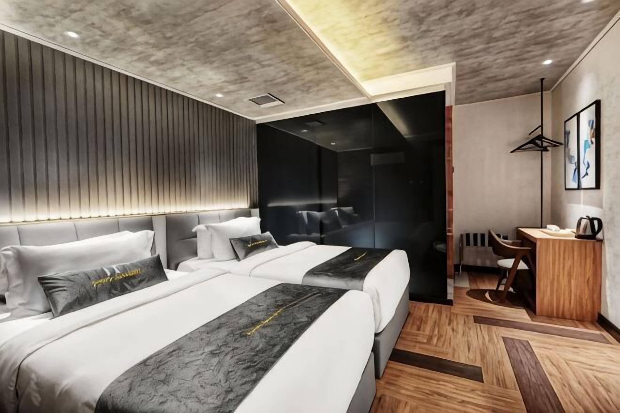 A modern hotel room with two beds, a desk, and a seating area.
