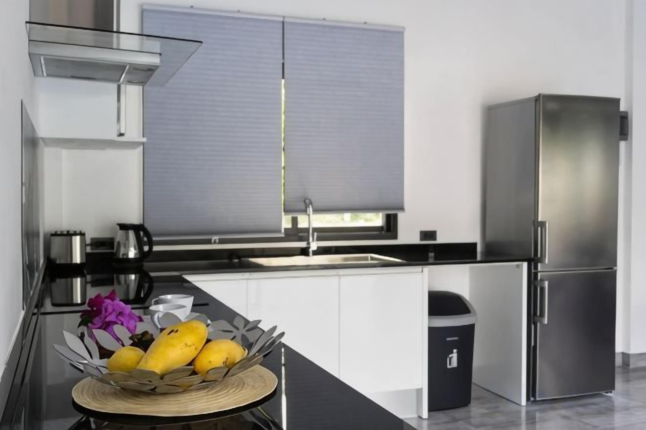 Une cuisine moderne équipée d’un réfrigérateur en acier inoxydable, d’un évier et d’une fenêtre avec des stores.