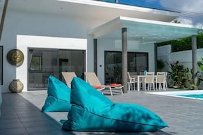 Un espace extérieur moderne, aménagé avec des coussins, une piscine et une entrée avec une porte en verre.