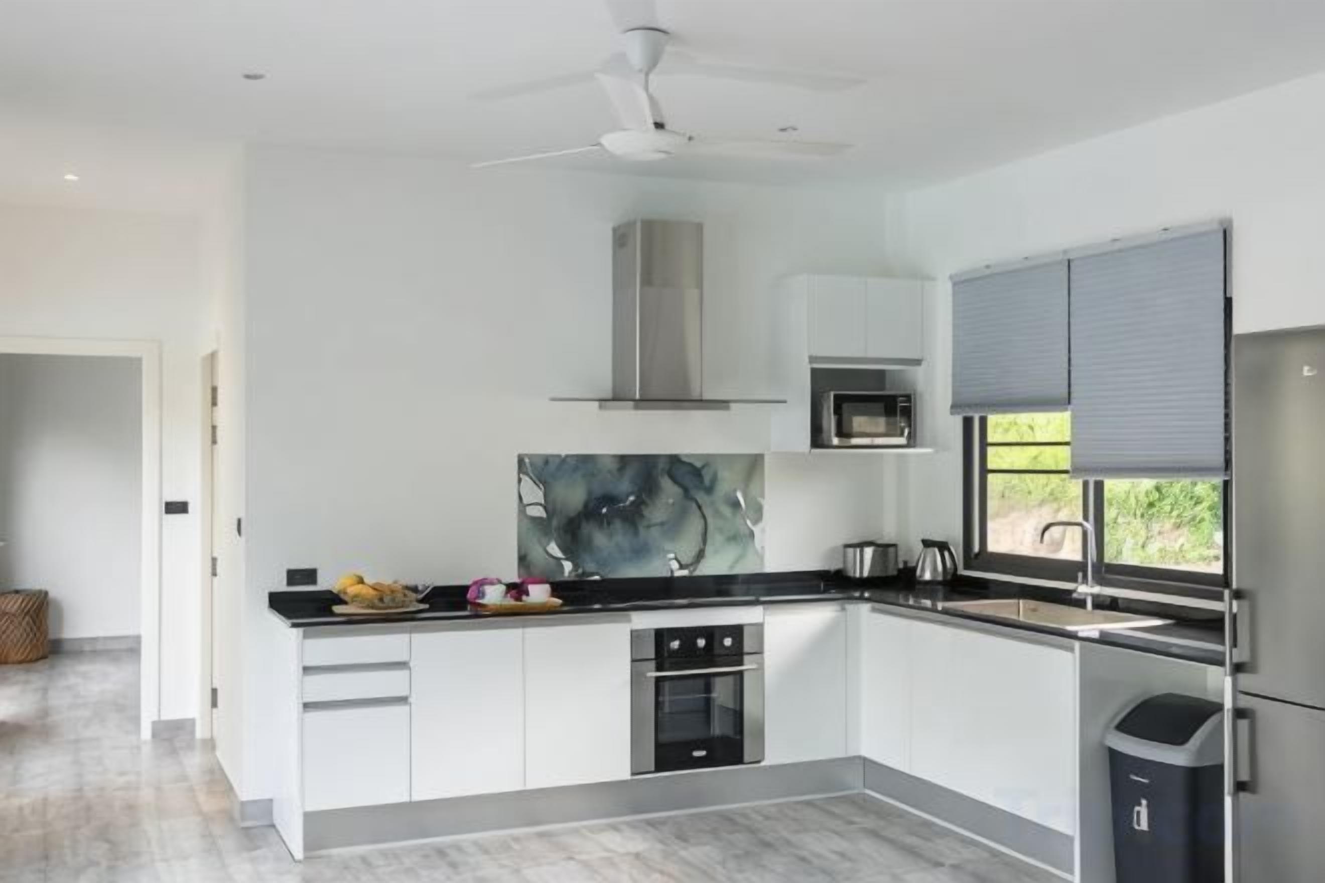A modern kitchen with white cabinets, a black countertop, a stainless steel range hood, and a window with blinds.