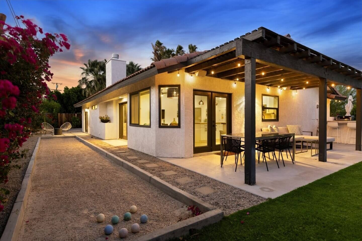 Une maison moderne dotée d’un patio couvert, d’une cuisine ouverte sur le salon grâce à des portes vitrées et d’un jardin bien entretenu.