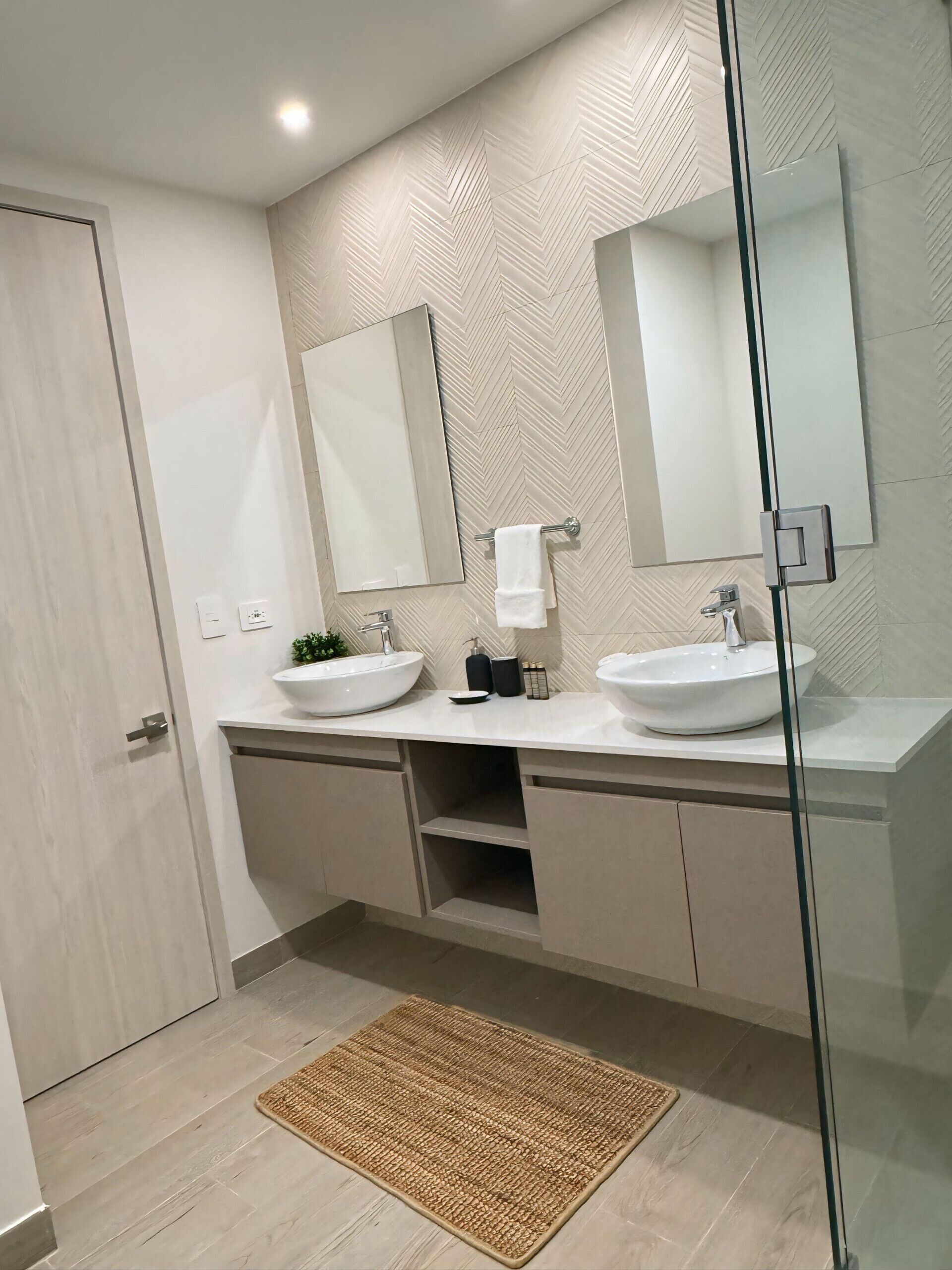 A modern bathroom with two sinks, a large mirror, and a herringbone-patterned wall.