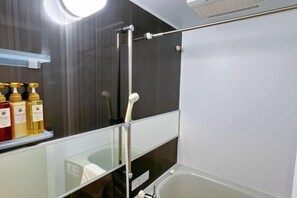 A modern bathroom with a glass shower enclosure, a white bathtub, and a shelf with toiletries. - AKATSUKI Nipponbashi(formeril Hotel Arashi Nipponbashi East No.8111) (Osaka)