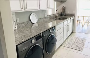 A modern kitchen with granite countertops, a built-in washing machine, and white cabinetry. - +Guard Gated Golf Course Front 1mi to Vegas Strip, Quiet Secure best kept secret (Las Vegas)