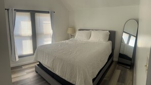 Ein Schlafzimmer mit einem Bett, einem Fenster mit Jalousien, einer Nachttischlampe und einem Spiegel.