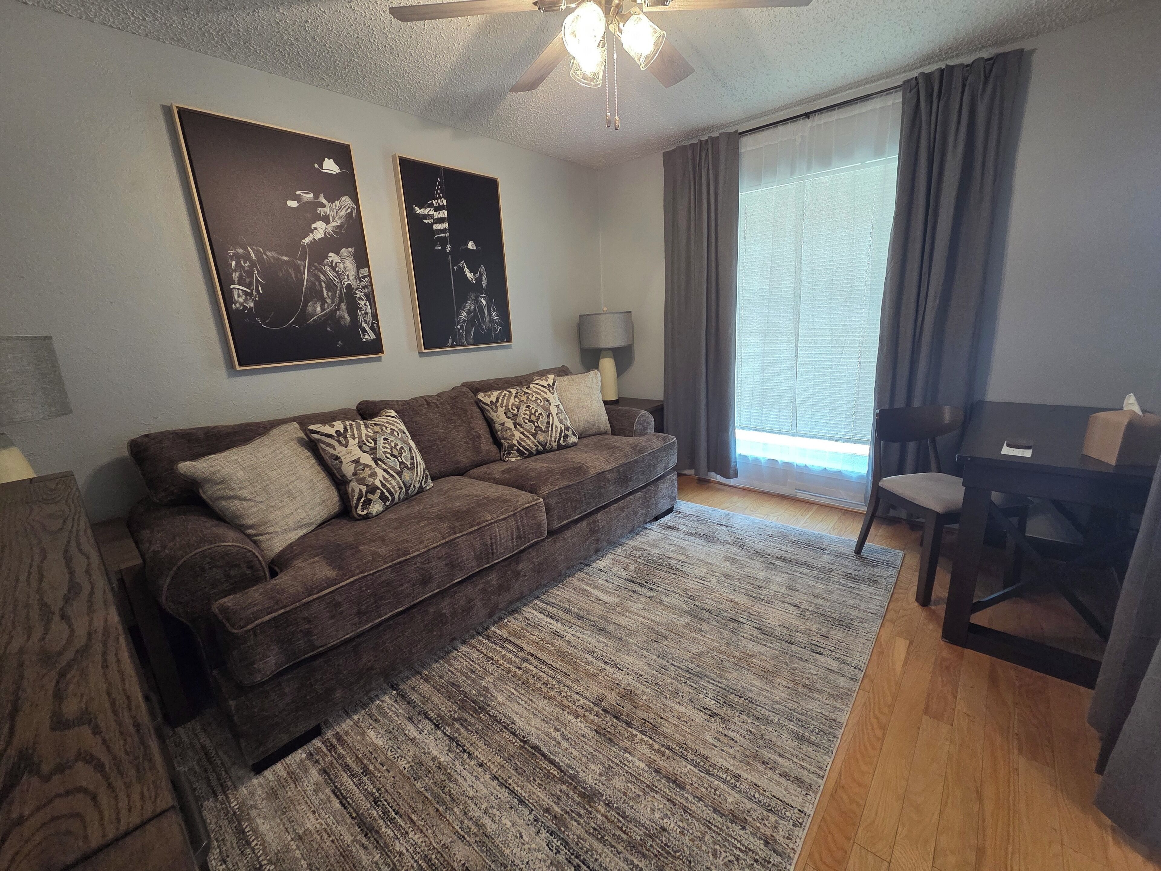 A living room with a brown sofa, patterned cushions, a wooden coffee table, a lamp, and a ceiling fan.
