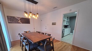 A dining room with a wooden table and chairs, a hanging light fixture, and a kitchen visible through an open door. - Cowboy Casa - DFW, AT&T Stadium, Stockyards (Hurst)