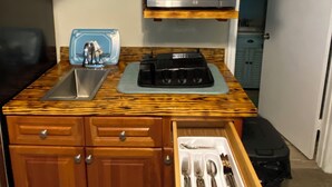 Una cucina compatta con mobili in legno, un forno a microonde, un lavello e un cassetto con posate.