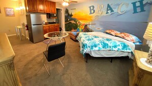 Una camera da letto con un murale raffigurante una spiaggia, un letto, una scrivania e un angolo cottura.