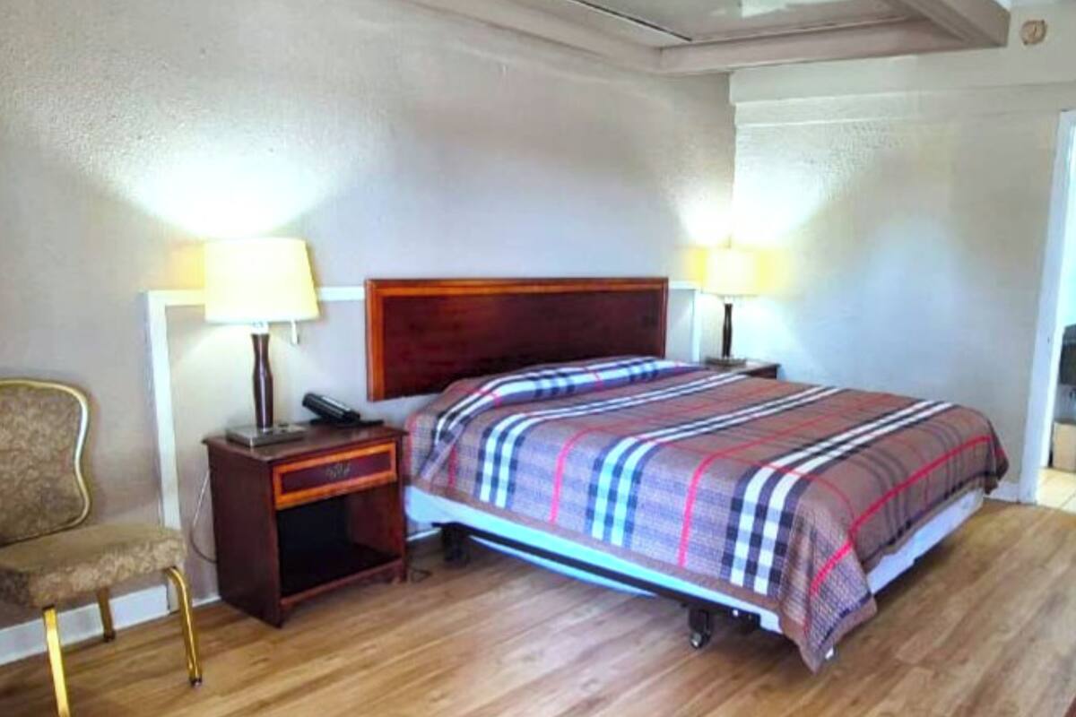 A hotel room with a wooden bed, two bedside lamps, a nightstand, and a chair.