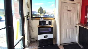 A room with a microwave on a counter, a door with a 'No Smoking' sign, and a window with a view of cars and trees. - Saratoga Motel By Capital O Near Midway Airport Chicago IL (Chicago)