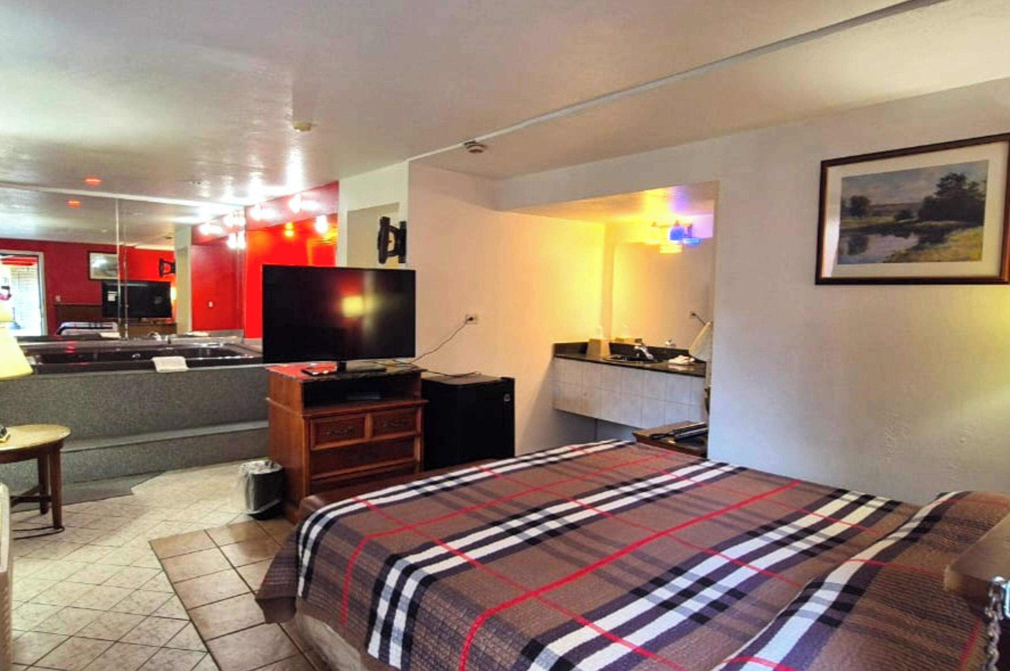 Quarto de hotel com cama, televisão, escrivaninha e cozinha compacta.