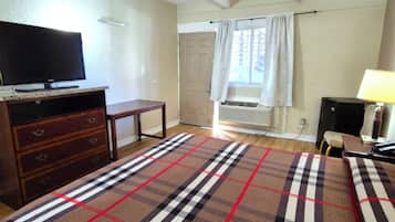 A bedroom with a bed, a television on a wooden stand, a small table, a lamp, and a window with curtains.