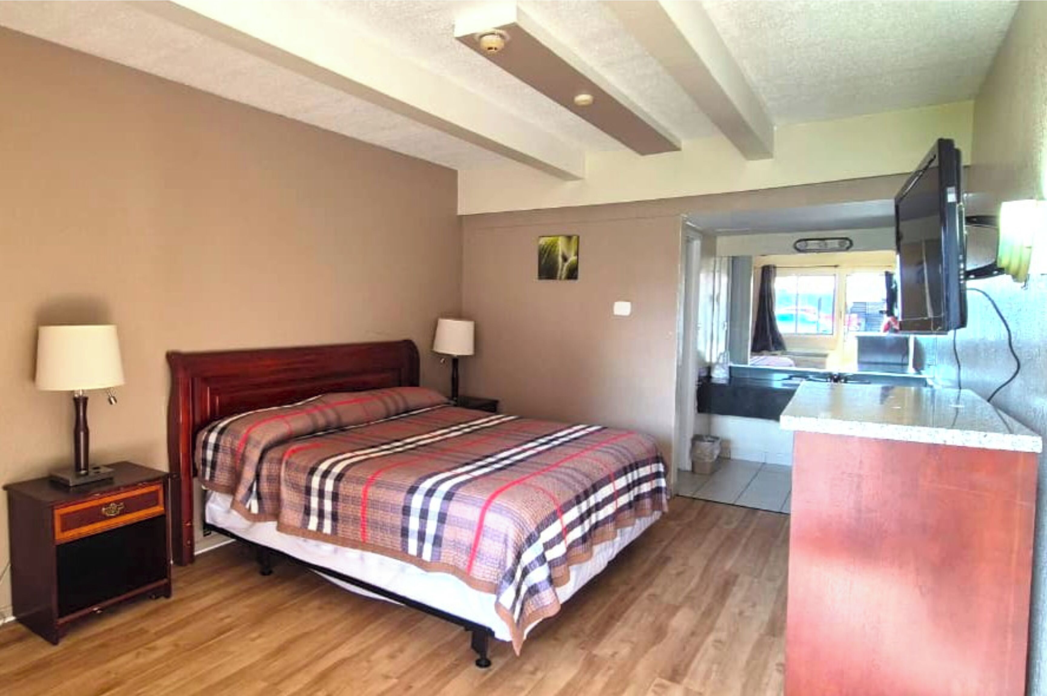 A bedroom with a wooden bed, bedside lamps, a small nightstand, and a television mounted on the wall.