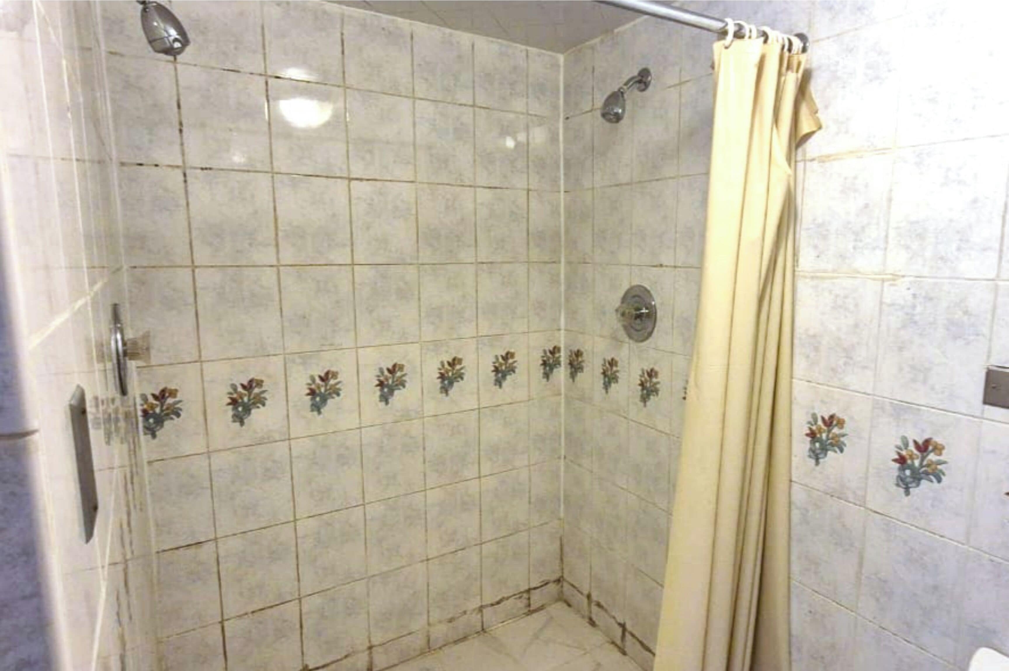Egy zuhanyzó, melynek a falai csempével vannak burkolva, zuhanyfej és zuhanyfüggöny található benne.