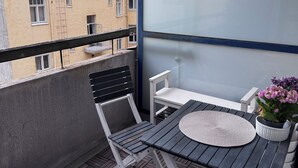 Een balkon met een tafel, stoelen, een bloempot en uitzicht op een gebouw.