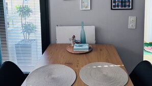 Een eetgedeelte met een houten tafel, twee geweven placemats, een vaas en lijstwerken aan de muur.