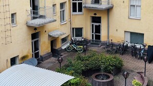 Een geel meerlaags gebouw met balkons, een binnentuin met plantenpotten en fietsen die er buiten staan.