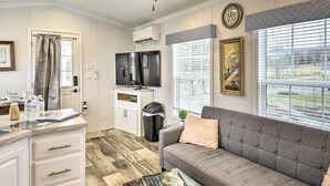 A modern living room with a grey sofa, a flat-screen TV, and a dining area with a white cabinet and a small table. - The Green Forest Refuge: Cabin & Suite (Pleasant Mount)