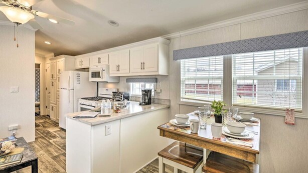 A kitchen with white cabinets, a central island, a dining table, and a ceiling fan. - The Green Forest Refuge: Cabin & Suite (Pleasant Mount)