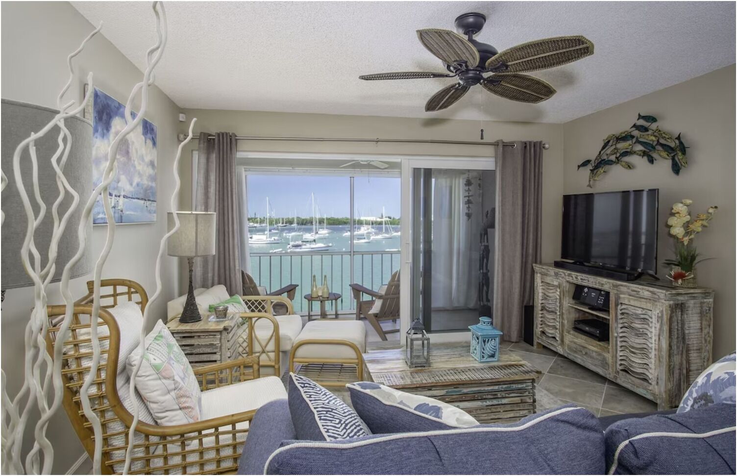 Een ruime woonkamer met een balkon met uitzicht op een jachthaven, ingericht met een bank, stoelen en een televisie.