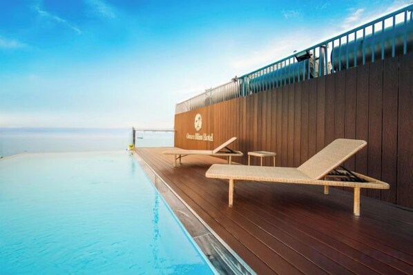 Una terraza con piscina, sillas de descanso y un muro de madera con un logotipo.