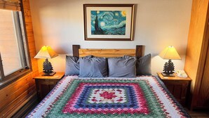 Ein ordentlich bezogenes Bett mit einer farbenfrohen Steude, einem hölzernen Kopfteil, zwei Nachttischlampen und einem gerahmten Kunstwerk darüber.