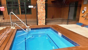 Ein rechteckiges Whirlpool mit einer Holzterrasse, umgeben von einem Metallzaun und einer Backsteinmauer.