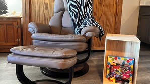 Ein modernes Wohnzimmer mit einem Ledersofa und Hocker, einer Zebra-Decke und einer Holzkommode mit einem Puzzlekästchen mit Punkten.